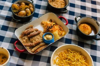 Traditional Bavarian meal featuring sausages, potatoes, cabbage, and mustard served on a checkered tablecloth.