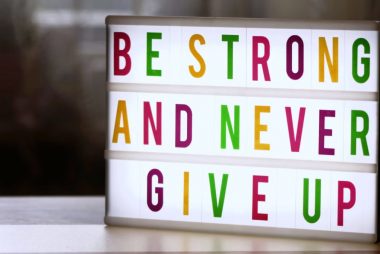 Motivational lightbox sign displaying 'Be Strong and Never Give Up.'